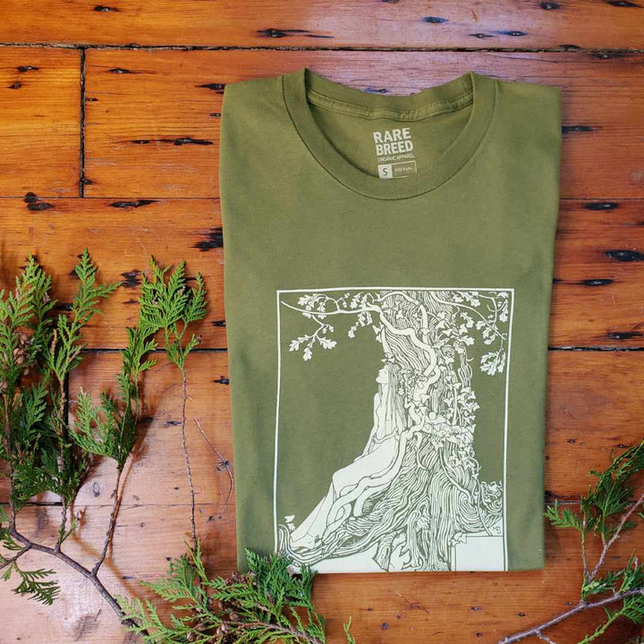 Rare Breed Organic T-Shirt made of 100% Organic Cotton featuring vintage dryad image.   This white screen print of a historical image shows a young woman leaning against an oak tree in a dream-like pose.  The folded T-shirt is olive green and is placed against a natural wood backdrop.  The neck tag reads: Rare Breed Organic Apparel.  Made in USA