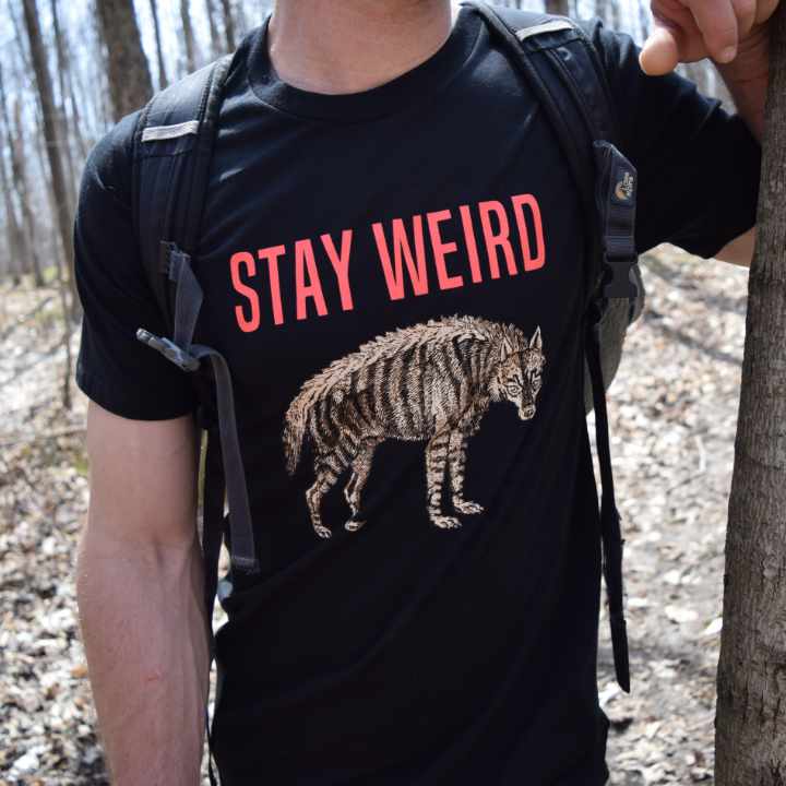 Outdoorsy dude wearing an organic cotton T-shirt, leaning against a tree. "Stay Weird" design by Rare Breed Organic Apparel.