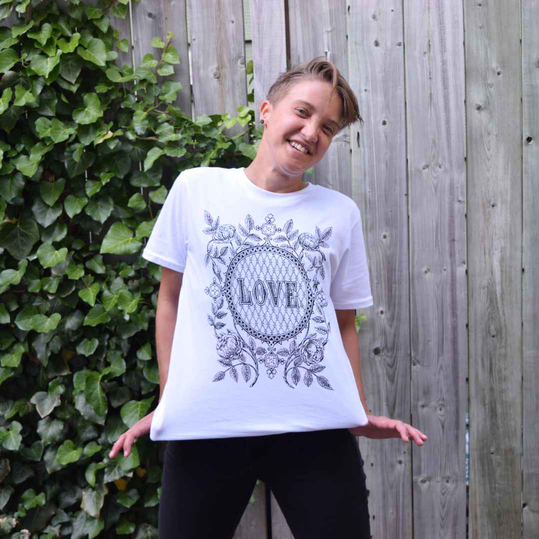 Women's organic T-shirt / Gender-neutral T-shirt by Rare Breed Organic Apparel.  White T-shirt with black love emblem.  Worn by a smiling woman in a natural outdoor setting.