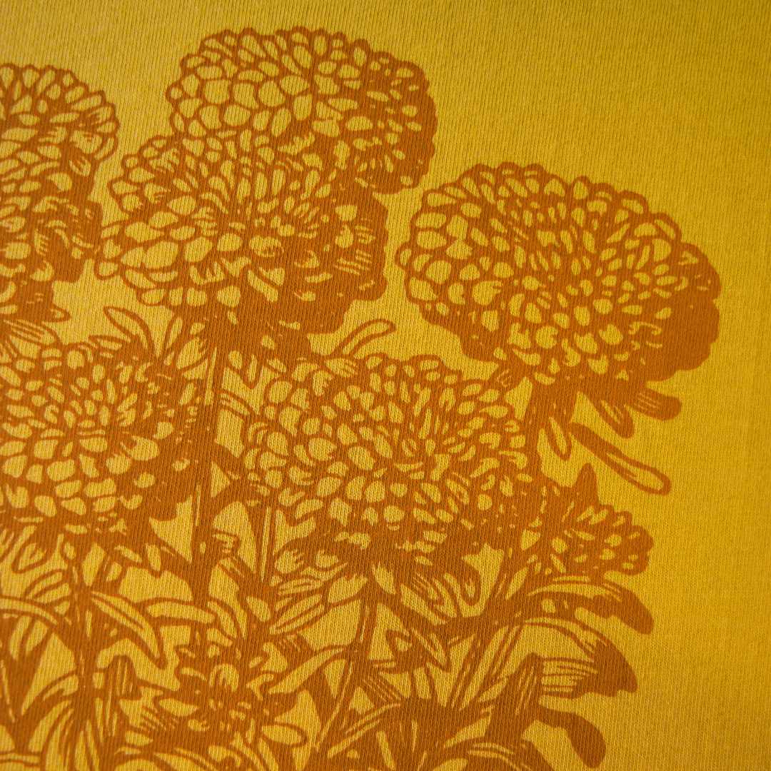 Close up of rust colored marigolds on a mustard T-shirt by Rare Breed Organic Apparel.