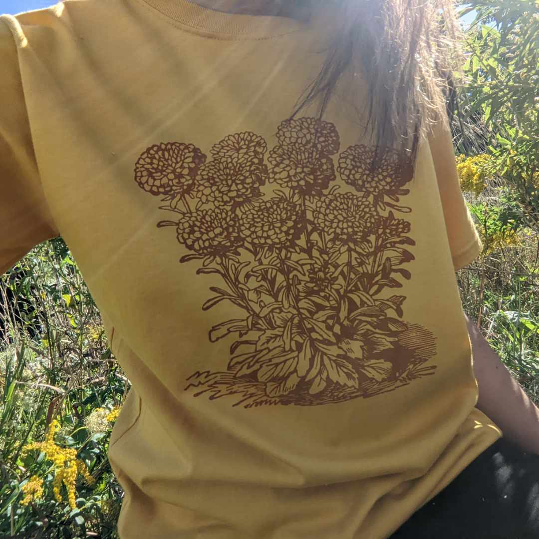 Woman wearing Rare Breed's gold and rust organic cotton T-shirt in a natural outdoor garden.  The perfect gift for a garden-lover!