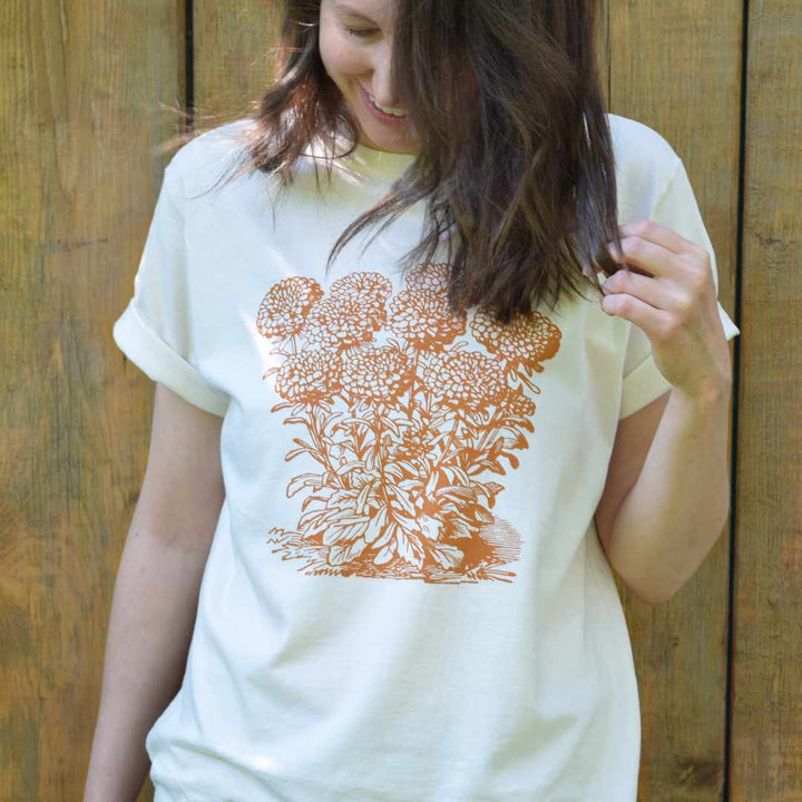 Woman wearing cream-coloured sustainable t-shirt with rust coloured marigold screenprint.  The image on this graphic tee was restored from a historical woodcut illustration by Canadian small business Rare Breed Organic Apparel.